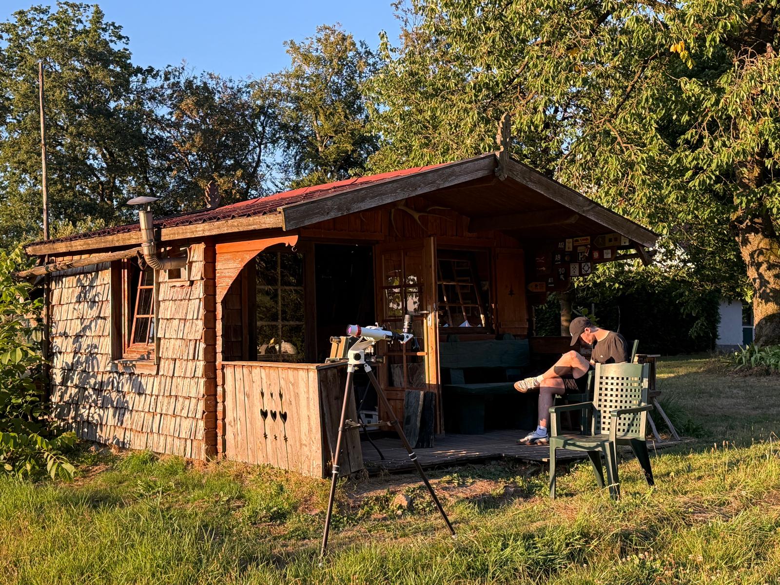 Fernrohr auf einem Stativ vor einer Gartenhütte im Abendlicht